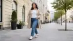 Kobieta w jeansach, trenczu i biało-czarnych sneakersach w stylu adidas Samba